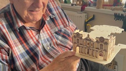 Blind veteran Maurice is looing at his model creation and smiling while sitting in a chair