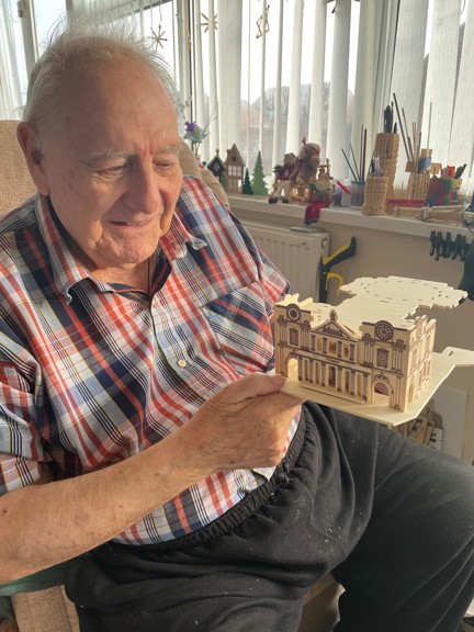 Blind veteran Maurice is looing at his model creation and smiling while sitting in a chair