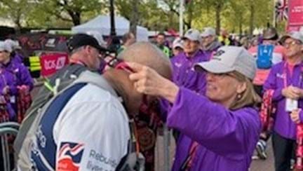 Naz with his head bowed down while a woman from the London Marathon team places his medal over his head