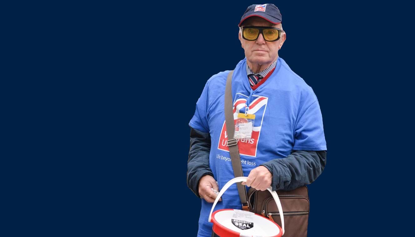 A photo showing blind veteran and volunteer Kenneth holding a collection bucket