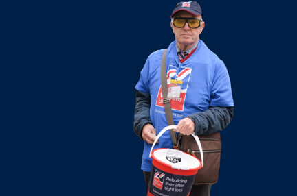 A photo showing blind veteran and volunteer Kenneth holding a collection bucket