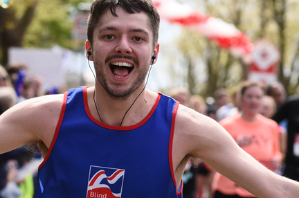 Supporter Alex, running a marathon in a Blind Veterans UK vest, smiling with his arms held out in celebration.
