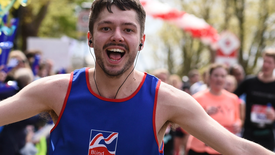Supporter Alex, running a marathon in a Blind Veterans UK vest, smiling with his arms held out in celebration.