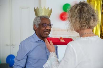 A woman handing a wrapped gift to a man wearing a Christmas hat 