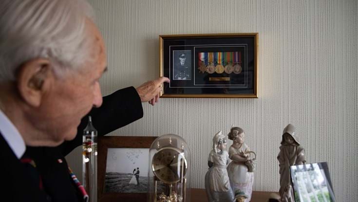 Blind veteran Ron pointing at his framed medals on the wall in his home