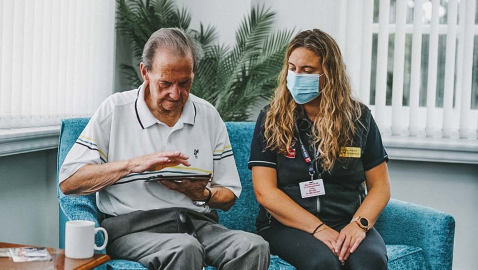 Blind veteran veteran Fred using a tablet, while sitting on a sofa with a Blind Veterans UK staff member