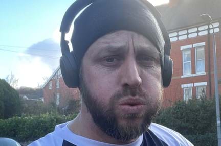 Matt wearing a Blind Veterans UK T-shirt and headphones at the end of a training run looking tired