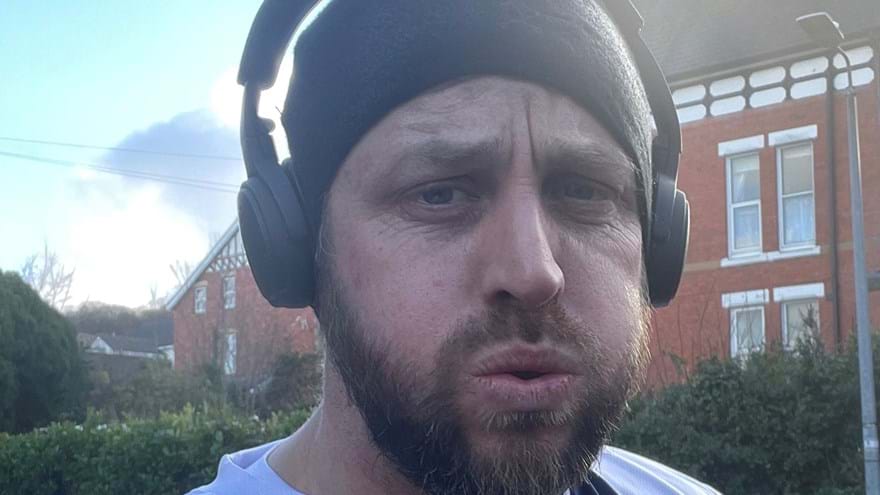 Matt wearing a Blind Veterans UK T-shirt and headphones at the end of a training run looking tired