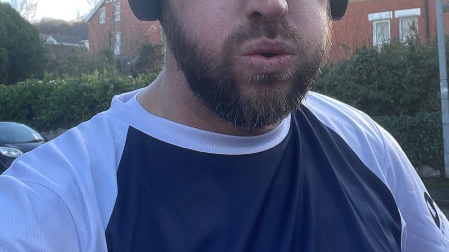 Matt wearing a Blind Veterans UK T-shirt and headphones at the end of a training run looking tired