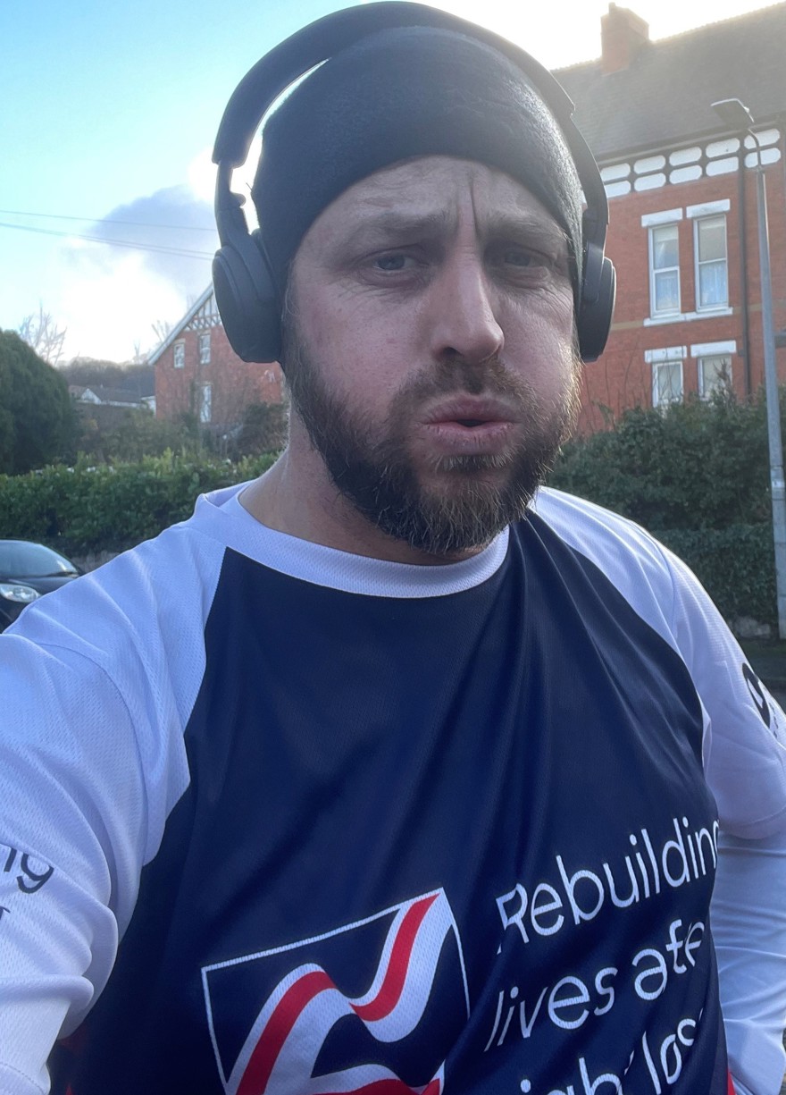 Matt wearing a Blind Veterans UK T-shirt and headphones at the end of a training run looking tired