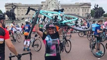 Emilia lifting her bicycle in the air with Buckingham Palace behind her