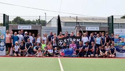 Participants from Yate Hockey Club's President's Day sat at the side of the pitch holding their hockey sticks and a Blind Veterans UK banner