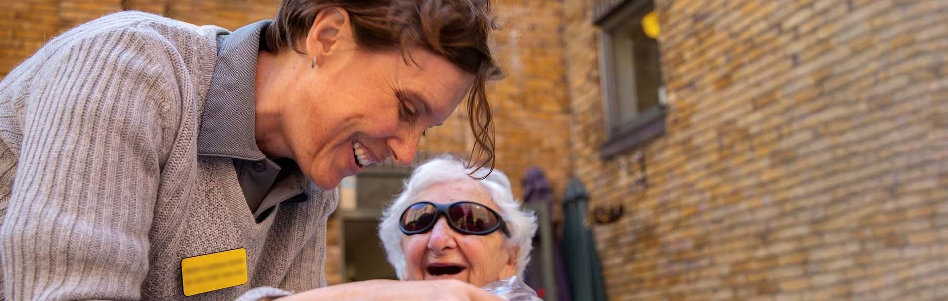 Blind veteran Connie, wearing dark sunglasses and laughing as she speaks to Blind Veterans UK staff member