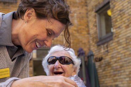 Blind veteran Connie, wearing dark sunglasses and laughing as she speaks to Blind Veterans UK staff member