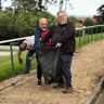 Mark holding open a black bin bag while colleagues place weeds inside