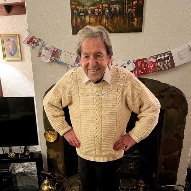 Blind veteran Elwyn stands in front of the fire place, with a Christmas decoration around his neck