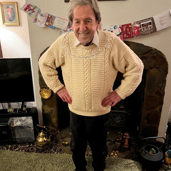 Blind veteran Elwyn stands in front of the fire place, with a Christmas decoration around his neck