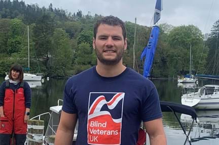 Johnny in a Blind Veterans UK t-shirt, standing near open water