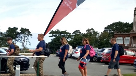 Five members of the Capita Army Recruitment team walking in a line. One walker is holding a very large Blind Veterans UK flag