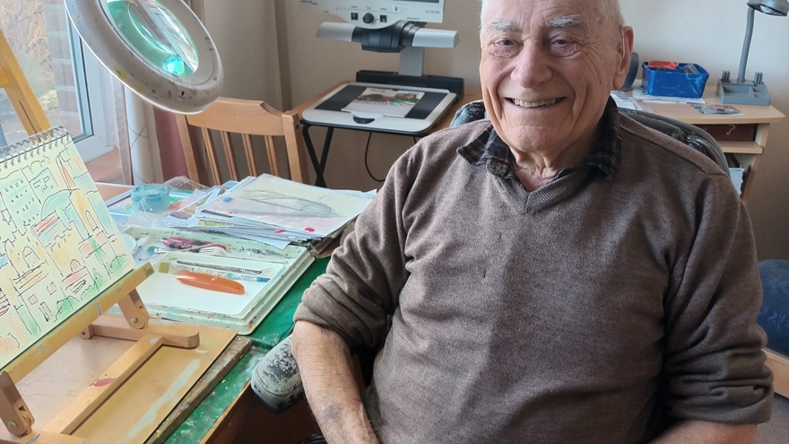 A photo of blind veteran Bill, pictured smiling and sitting next to his artwork