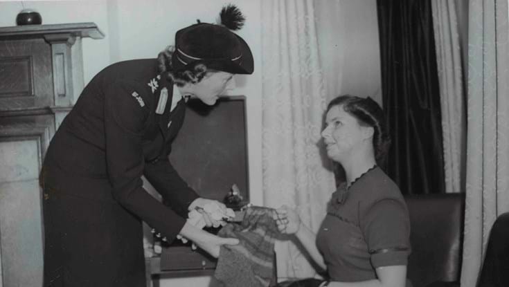 An archive photograph of blind veteran Barbara showing a woman in uniform her sewing work
