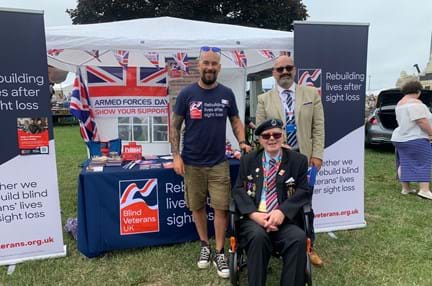 A Blind Veterans UK display stand set up with leaflets and posters with members of staff and blind veteran David stood in front 