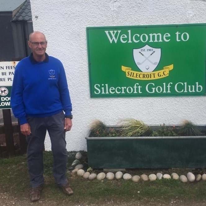 Charity supporter David, standing next to a large green sign that reads: Welcome to Silecroft Golf Club