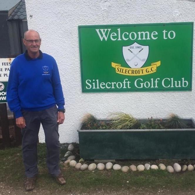 Charity supporter David, standing next to a large green sign that reads: Welcome to Silecroft Golf Club