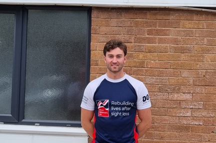 James stood wearing his Blind Veterans UK t shirt in front of a sign for Gwynedd Forklifts