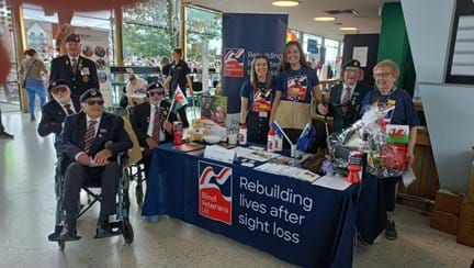 Table with leaflets and Blind Veterans UK items set up inside with staff and veterans around it