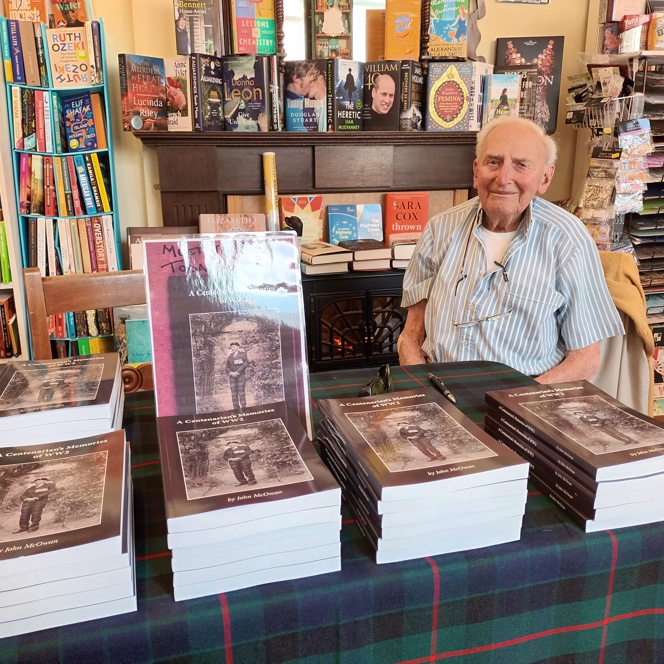 Blind veteran John, sitting at a table with piles of books stacked in front of him