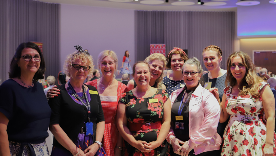 A group of nine Blind Veteran UK staff members at an event, gathered together and smiling