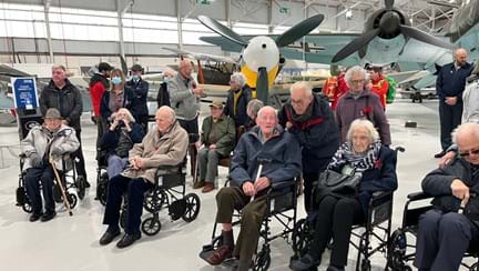 A photo of a group of blind veterans visiting the RAF Cosford Museum posed in front of the fighter jets