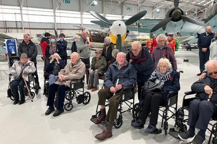 A photo of a group of blind veterans visiting the RAF Cosford Museum posed in front of the fighter jets