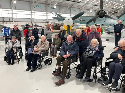 A photo of a group of blind veterans visiting the RAF Cosford Museum posed in front of the fighter jets