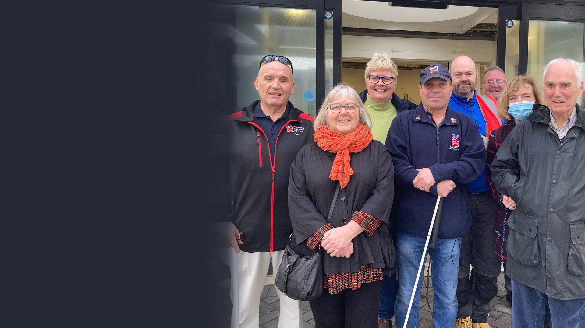 A group of blind veterans smiling for a photograph outside the new Rustington Centre of Wellbeing after their visit