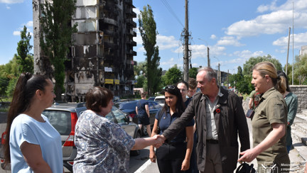 Nick Caplin, shaking hands with a Ukrainian citizen, standing on the street in front of a damaged building