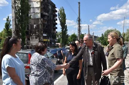 Nick Caplin, shaking hands with a Ukrainian citizen, standing on the street in front of a damaged building