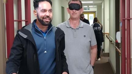A man wearing a blindfold is holding the arm of  another man while he is guided around the inside the the Llandudno Centre
