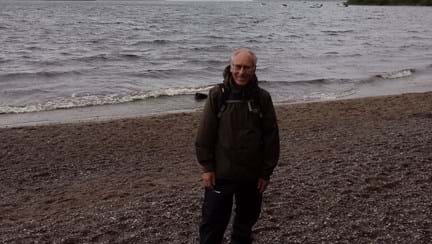 Gary pictured on a pebbled beach with the sea behind him on a cloudy day