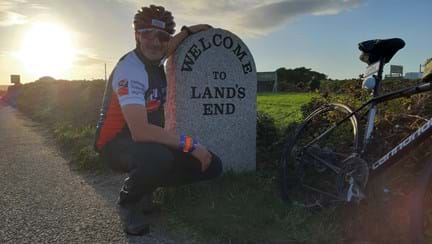 Jon crouched down next to a stone sign for Lands End