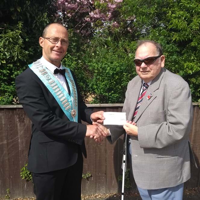 A blind veteran and a man shaking hands and holding up a cheque