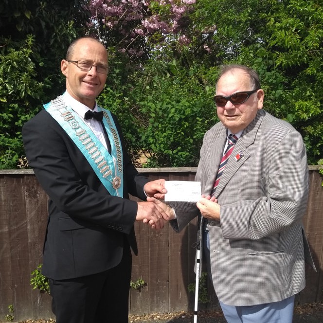 A blind veteran and a man shaking hands and holding up a cheque