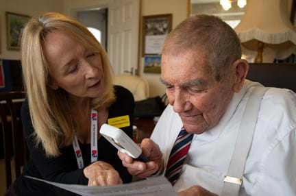 Blind veteran using an magnifier to read, with Community Support Worker at his side helping him