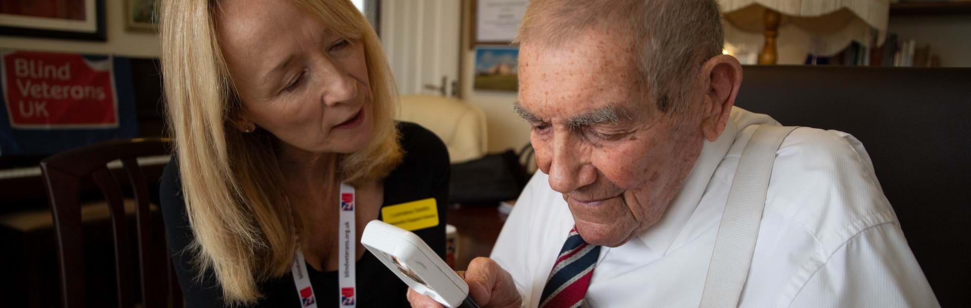 Photo of Eddie Gaines, blind veteran with Lorraine, Community Support Worker using an magnifier