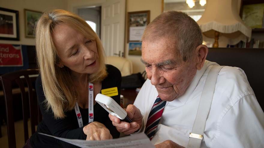 Photo of Eddie Gaines, blind veteran with Lorraine, Community Support Worker using an magnifier