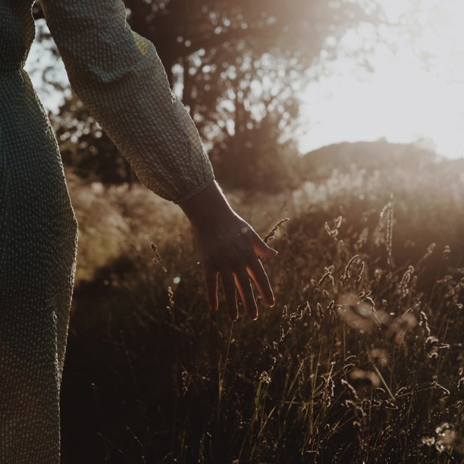 A photo of a person walking through grass during sunrise