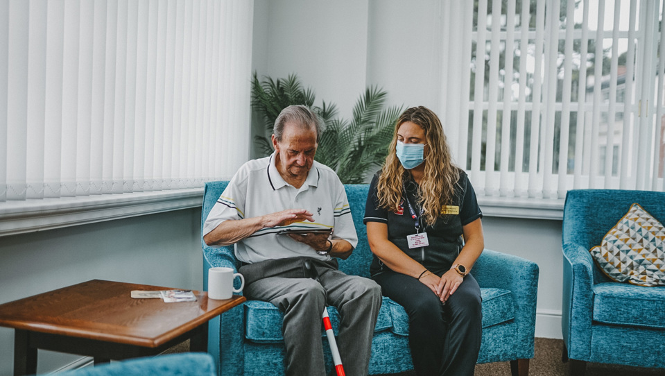 Blind veteran veteran Fred using a tablet, while sitting on a sofa with a Blind Veterans UK staff member