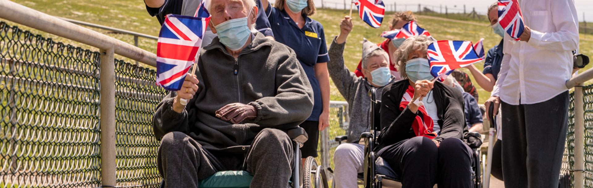 photo of a group of blind veterans celebrating VE day holding Union Jack flags and wearing face masks