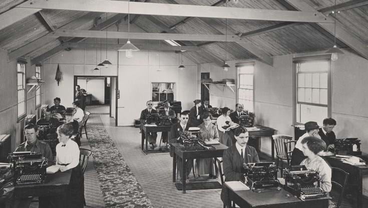 An archive photograph of a group of blind veterans and teachers sitting at desks with typewriters